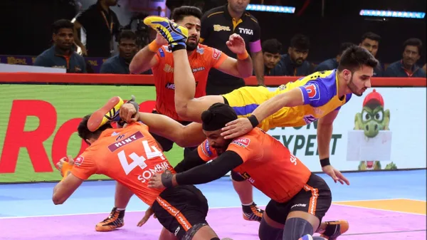 Pro Kabaddi League match action with defenders tackling a raider mid-air.